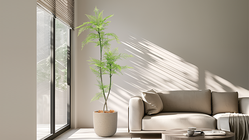 Artificial fern tree decor Tall artificial fern tree in a beige modern living room, near large glass windows with sunlight streaming in.