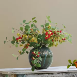 Artificial red and green berry branches in ceramic vase.