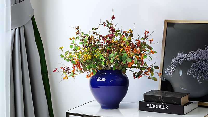 Artificial berry plant arrangement in a glossy blue vase, vibrant decor for modern interiors.