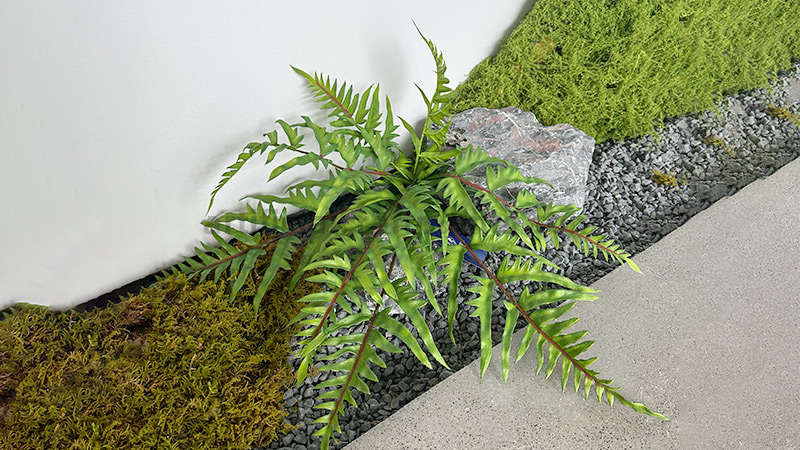 artificial fern with red stems planted in a bed of moss and gravel
