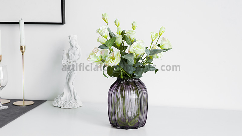 Artificial Lisianthus Bouquet A bouquet of white artificial lisianthus flowers in a ribbed purple glass vase.