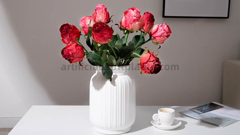 Artificial Red Roses A bouquet of red and pink artificial roses in a fluted white vase on a table.