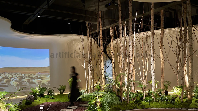 Indoor artificial forest with birch trees, ferns, and moss.