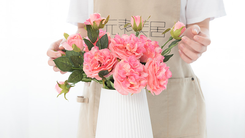 Pink and white artificial Eustoma flowers with green leaves on a white surface.